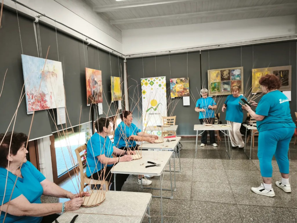 Skupina účastníčok v modrých tričkách na workshope tradičného pletenia z prútia v Jasienici