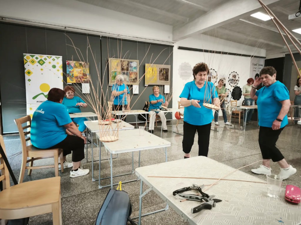 Účastníčky workshopu tradičného pletenia z prútia pri stoloch v Obecnom kultúrnom centre v Jasienici v rámci projektu Folkowe Pogranicze
