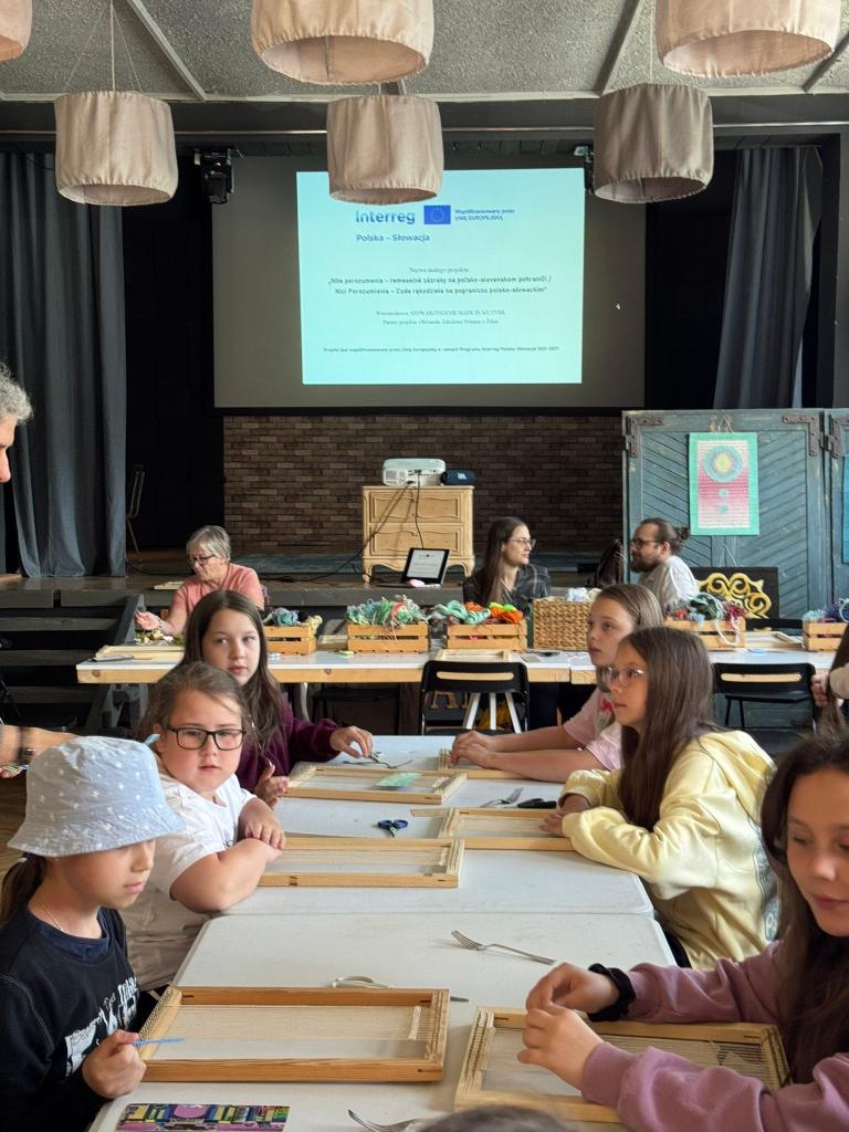 Deti pri tkáčskom workshope v Belej s plátnom projektu Interreg v pozadí