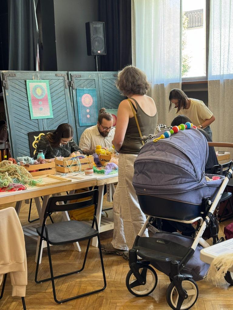 Účastníčky workshopu pri stole s farebnou vlnou a ukážkami tkanín v Belej