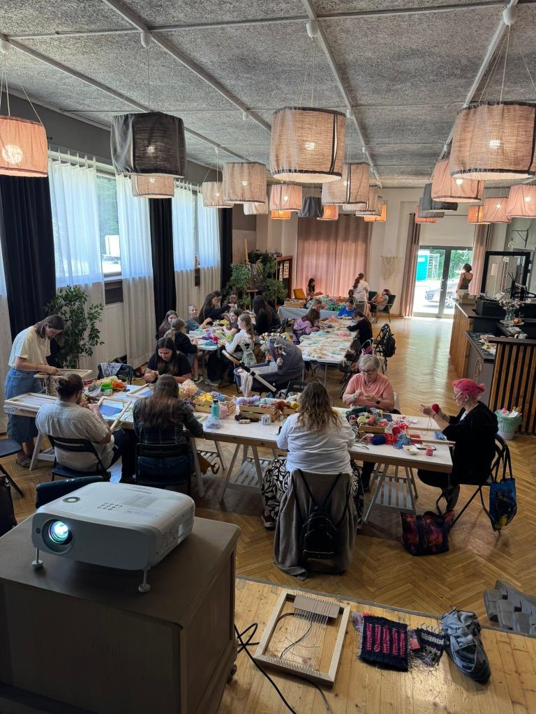 Široký záber na tkáčsky workshop s desiatkami účastníkov v sále v Belej