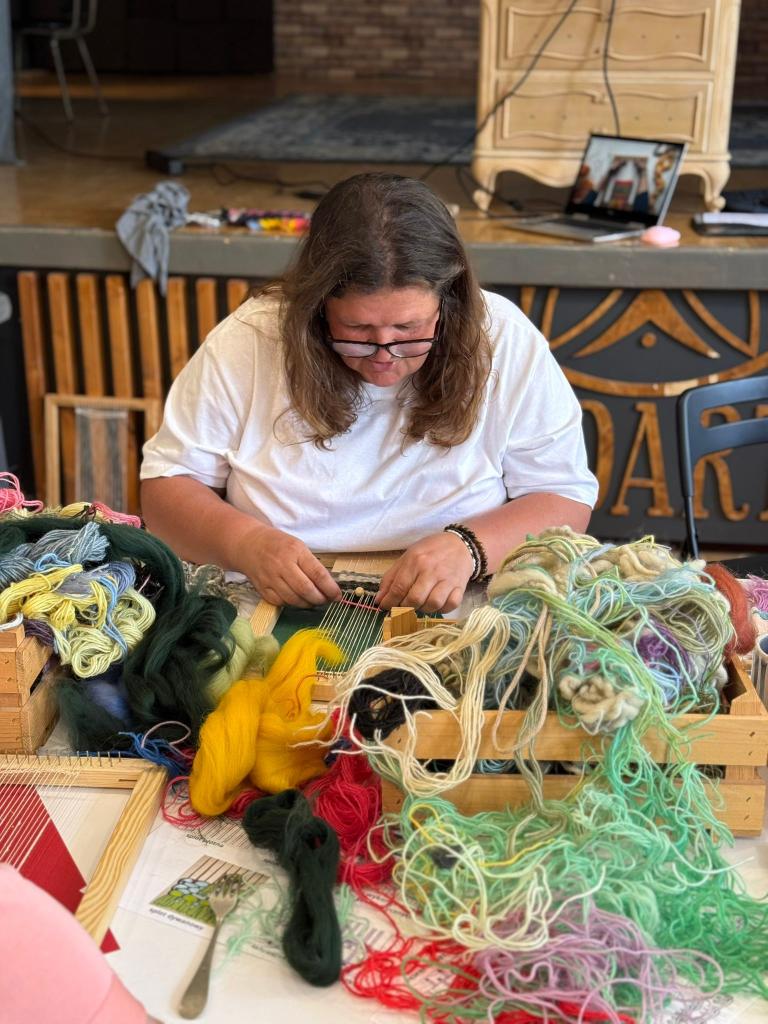 Účastníčka tká na drevenom ráme so zelenou vlnou počas workshopu v Belej